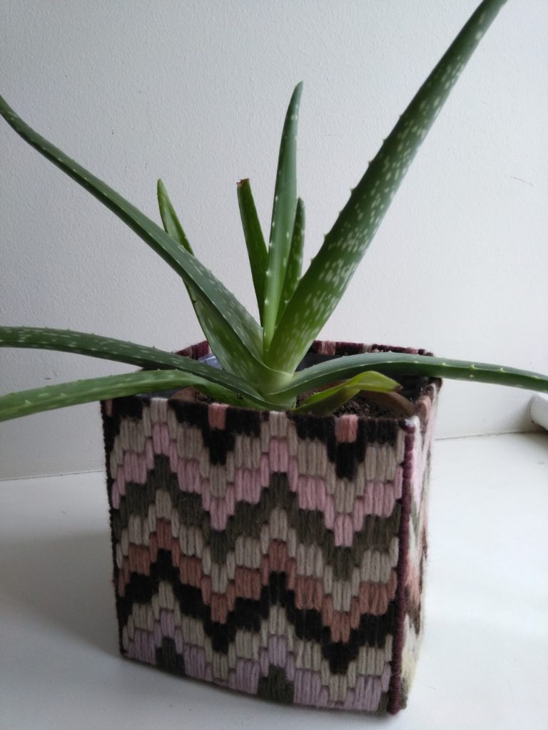 Plant pot made out of embroidery on plastic canvas and a lining of recycled plastic